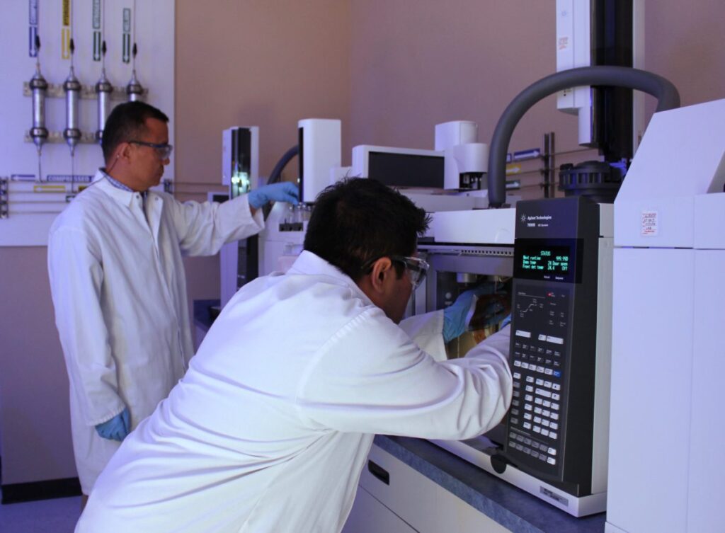 an image of two male lab workers in white lab coats working with some complex laboratory machines