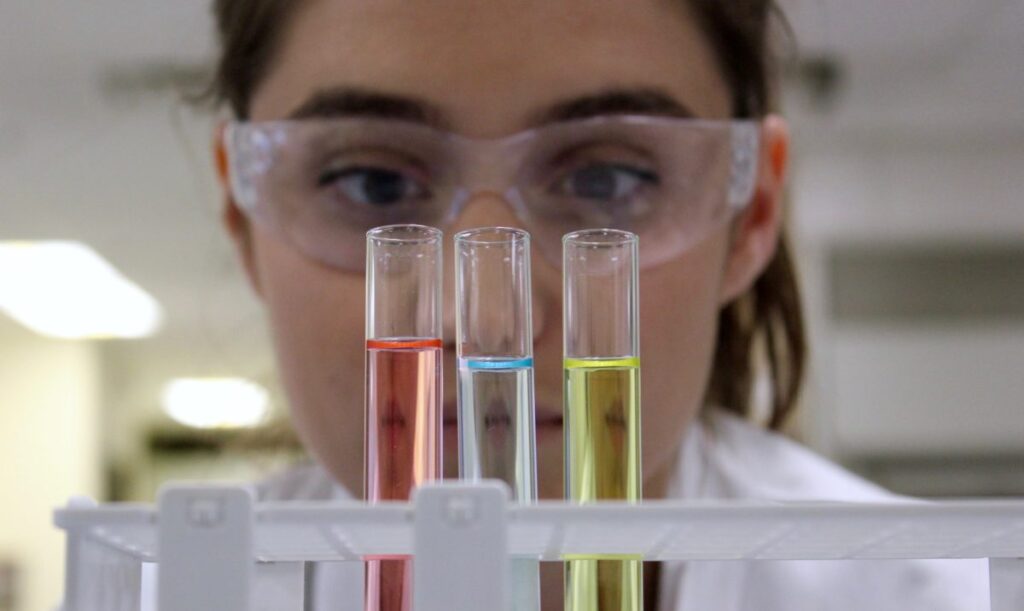 lab technician looking at three test tubes one red one blue one yellow